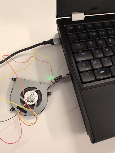 mnt reform laptop. A cable is hanging out the side. Connected to it is a small blue PCB, the PWM controller. Connected to that is a small fan, it is spinning.